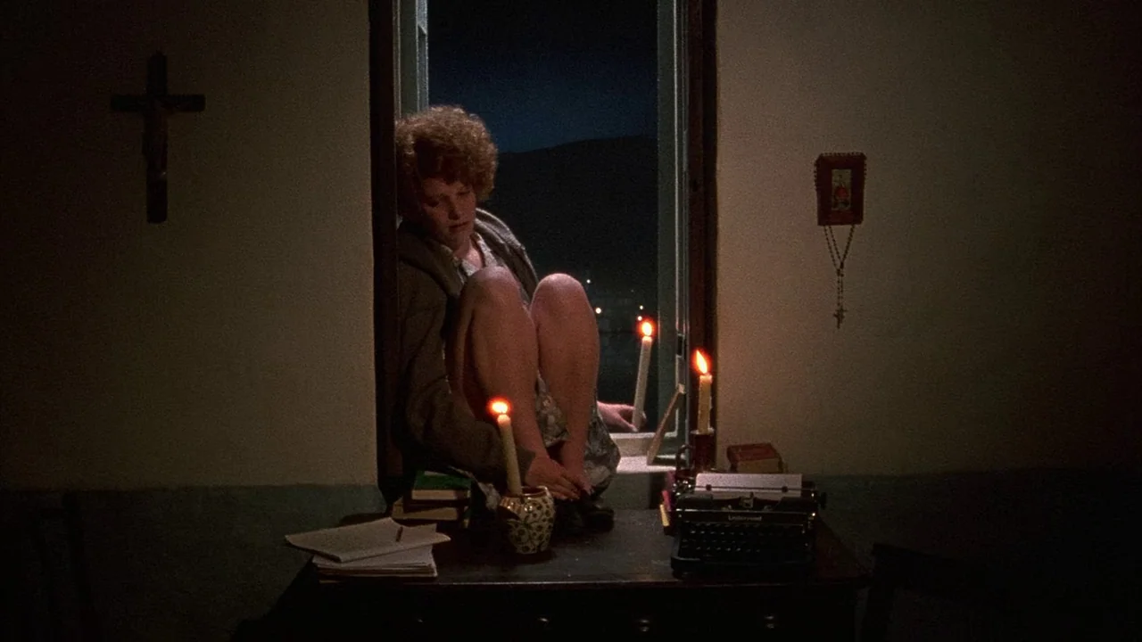An Angel At My Table (1990) movie still: medium — A dimly lit room at night features a crucifix and rosary on the wall. A woman sits on the edge of…