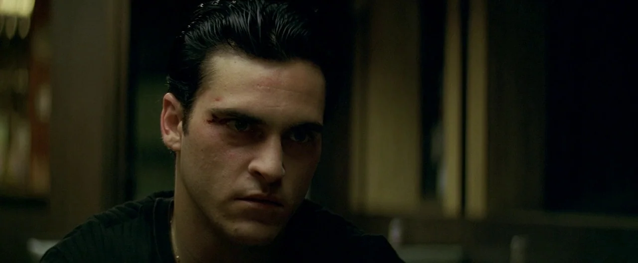 The Yards (2000) movie still: closeup — A dimly lit interior space with dark, muted tones and obscured background details. A young man with a facial…
