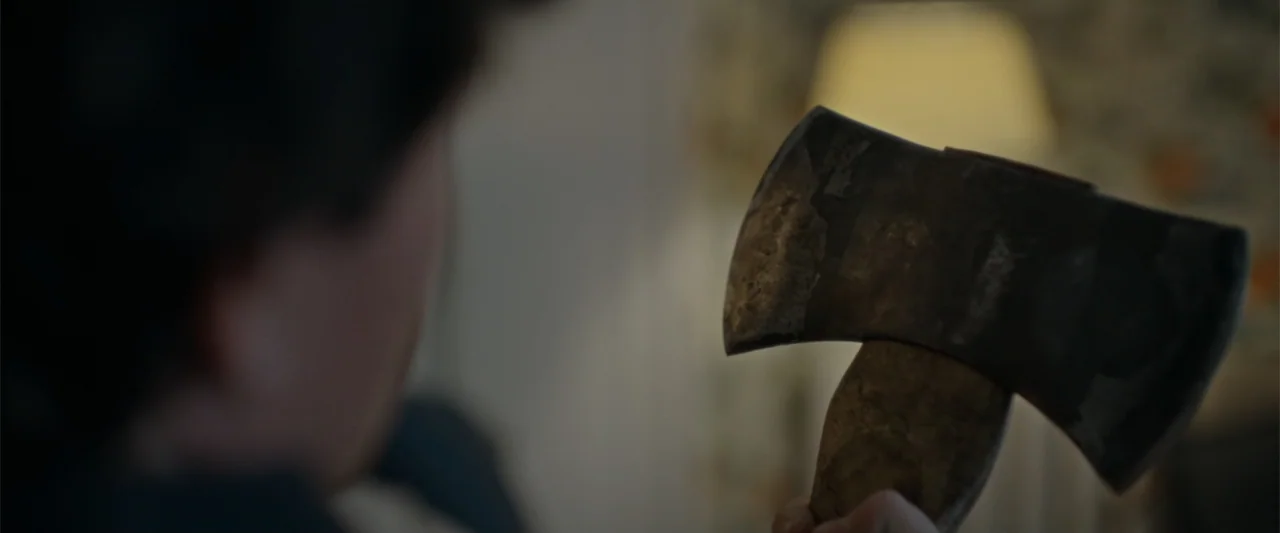 Silent Night, Deadly Night (2025) movie still: closeup — An interior space features a person holding an axe in the foreground. The person stands…