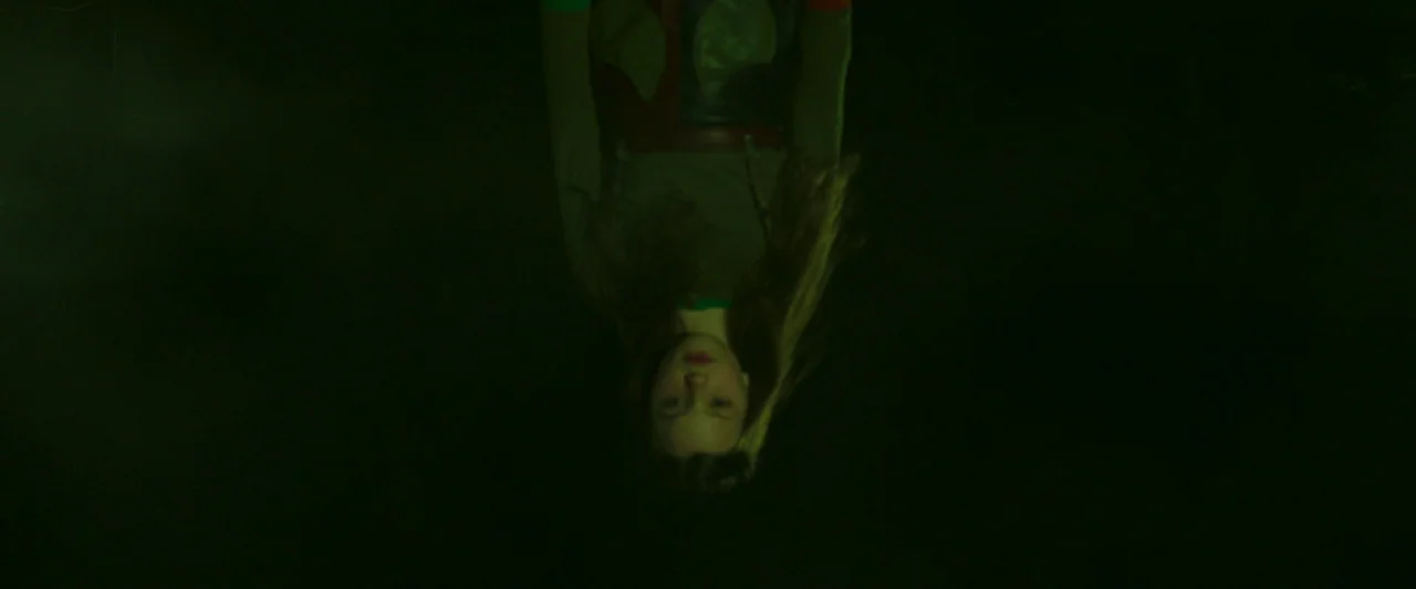Stopmotion (2024) movie still: medium — An inverted young woman is suspended in a dark, empty space. The subject is oriented upside down against a…