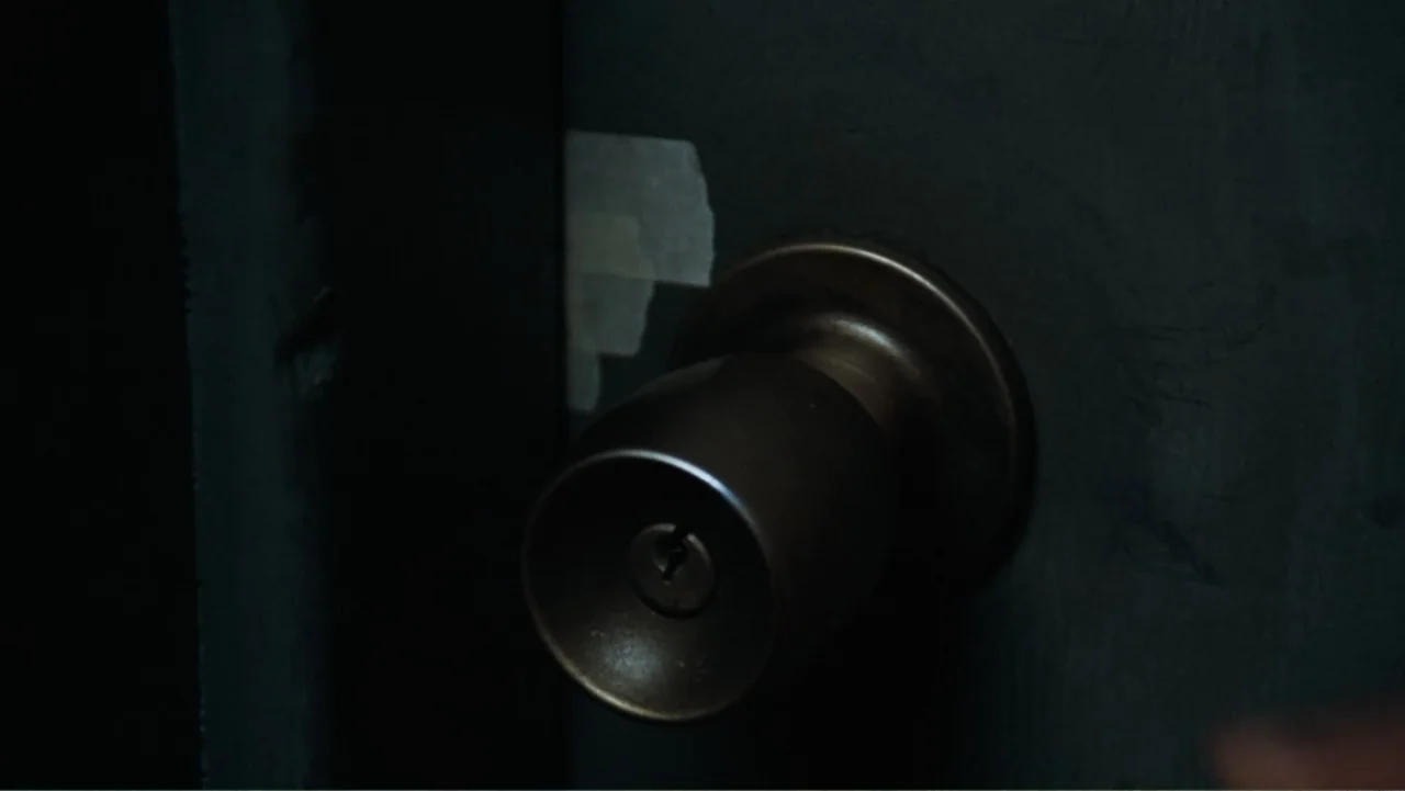 All the President's Men (1976) movie still: closeup — A close-up view of a matte black door with a circular brass doorknob. A piece of white…