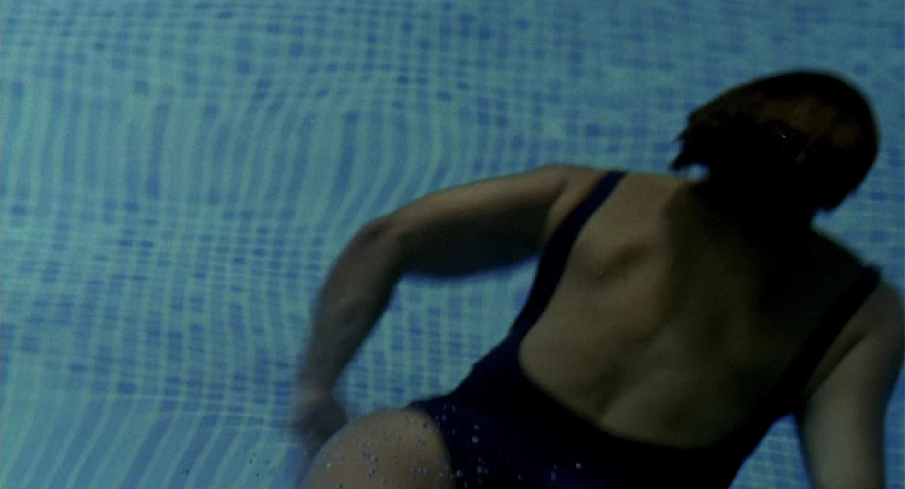 The Nameless (1999) movie still: medium — A person swims submerged in a blue pool with a tiled floor visible below. The swimmer moves with their…