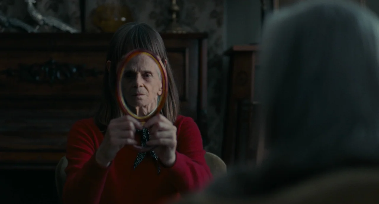 La Abuela (2021) movie still: medium — An interior living room with dark vintage wood furniture and patterned wallpaper in background. An elderly…