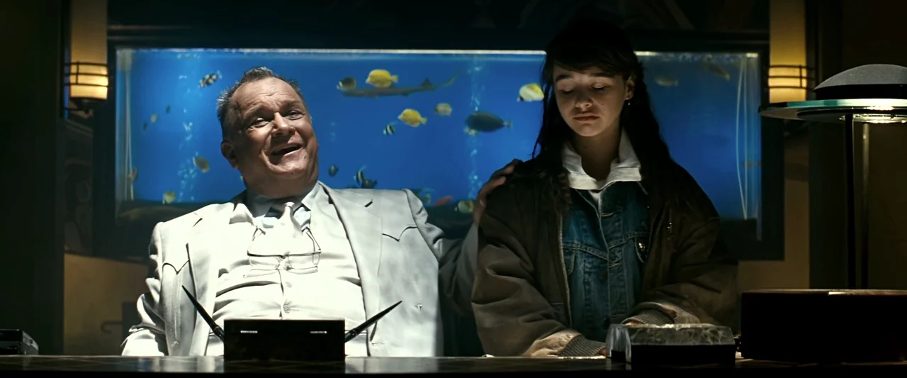 The Last Boy Scout (1991) movie still: medium — An office features a large glowing fish tank spanning the wall behind two people. The older man sits…