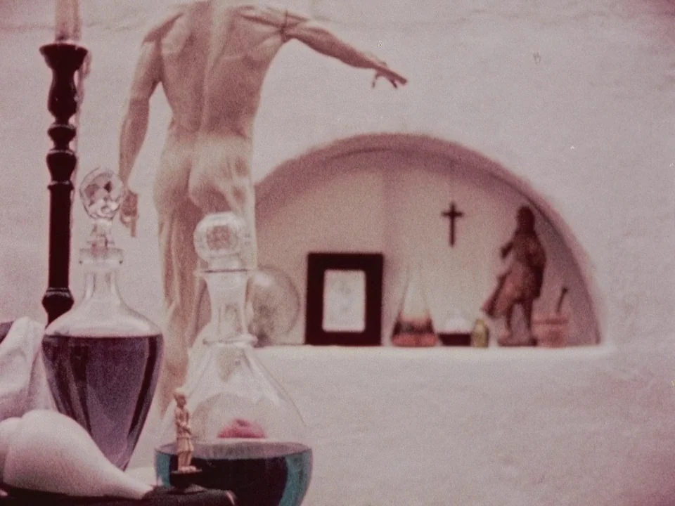 The Wormwood Star (1956) movie still: medium — A light-colored stone or plaster wall features an arched niche containing small decorative objects. A…