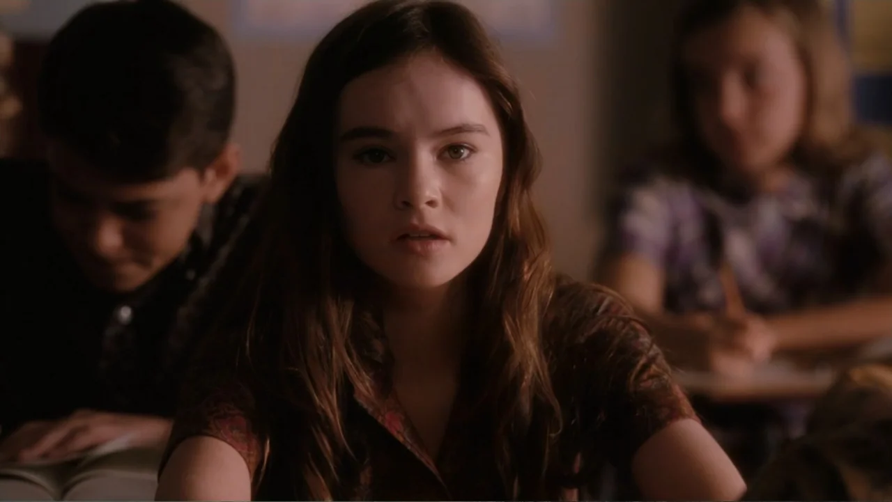 Flipped (2010) movie still: medium — A student sits at a desk in a dimly lit, quiet classroom environment. The teenage girl looks forward with her…