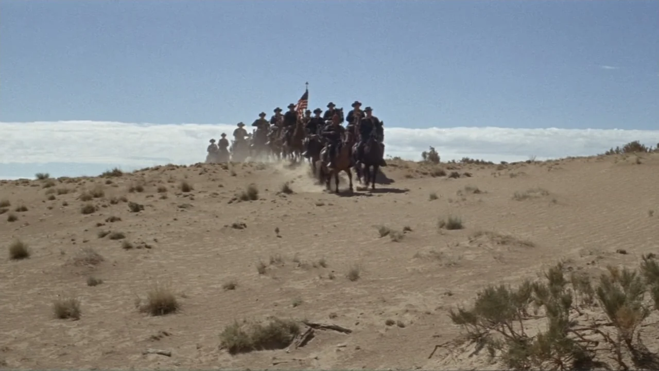 A Distant Trumpet (1964) movie still: wide — A vast, arid desert landscape features rolling sand dunes under a clear blue sky. A column of cavalry…