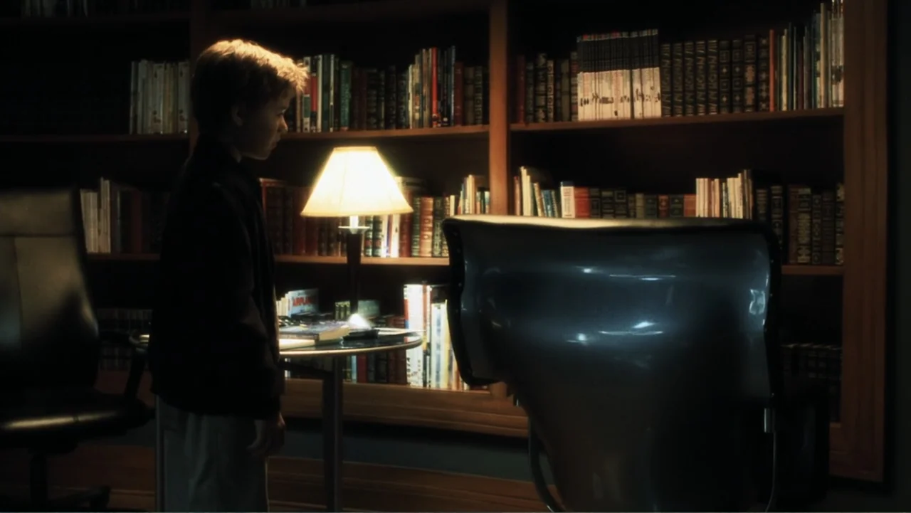 A.I. Artificial Intelligence (2001) movie still: medium — A home office features floor-to-ceiling bookshelves filled with books and a glass desk. A…
