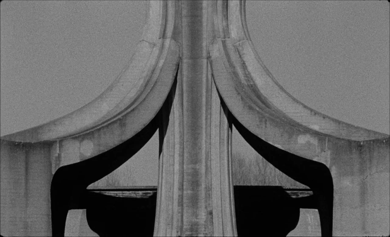 Last and First Men (2020) movie still: wide — A close structural detail of a brutalist concrete bridge pier with curved support beams. The heavy…