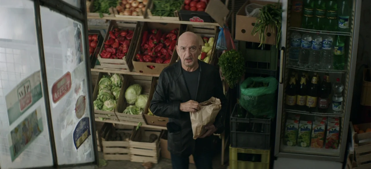 Morir un Poco (1967) movie still: medium — A small grocery store interior with wooden produce crates stacked with vegetables and fruit. An elderly…