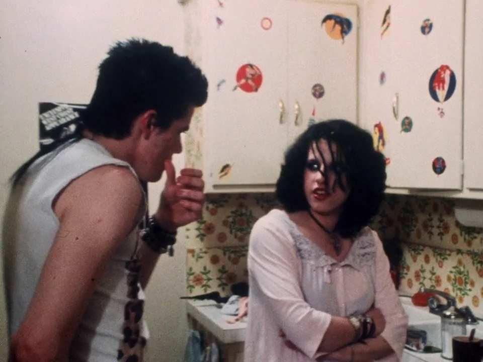 Decline of Western Civilization (1981) movie still: medium — A cramped kitchen features floral wallpaper and cupboards decorated with numerous small…