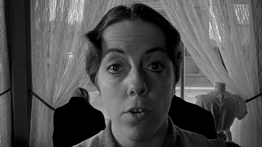 Paper Moon (1971) movie still: closeup — A shop window interior features sheer lace curtains and a background mannequin torso. A woman stands…