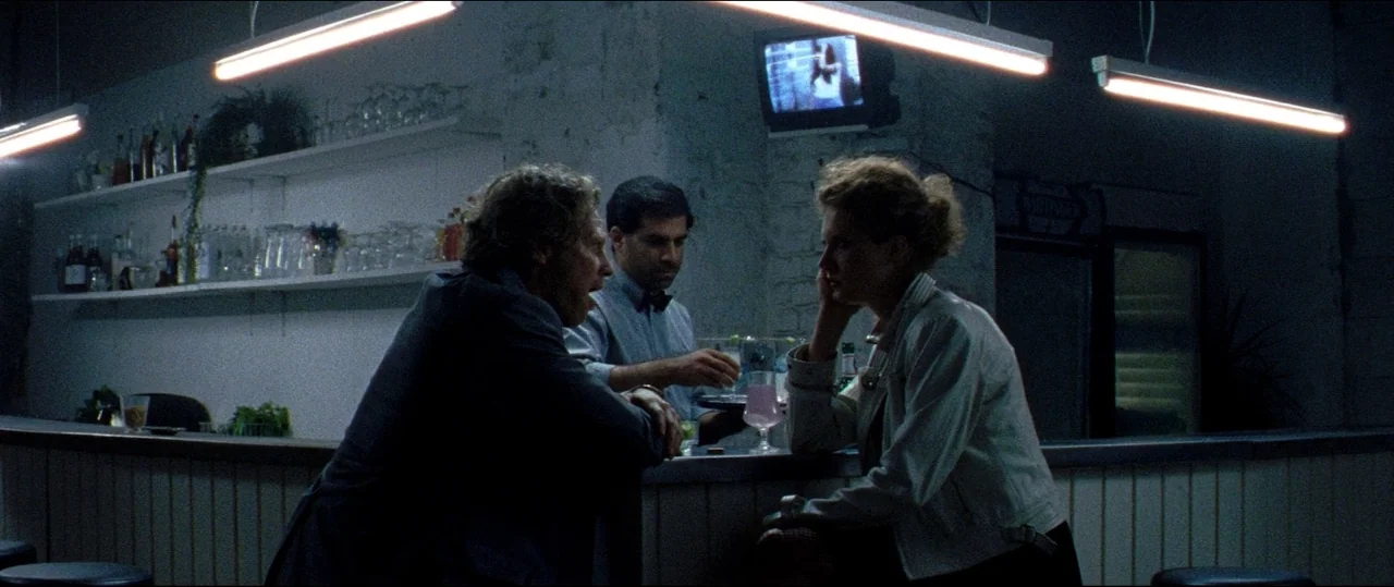 Luz (2018) movie still: medium — A dimly lit room features a long wooden counter and white-painted brick walls. Three people stand around the…