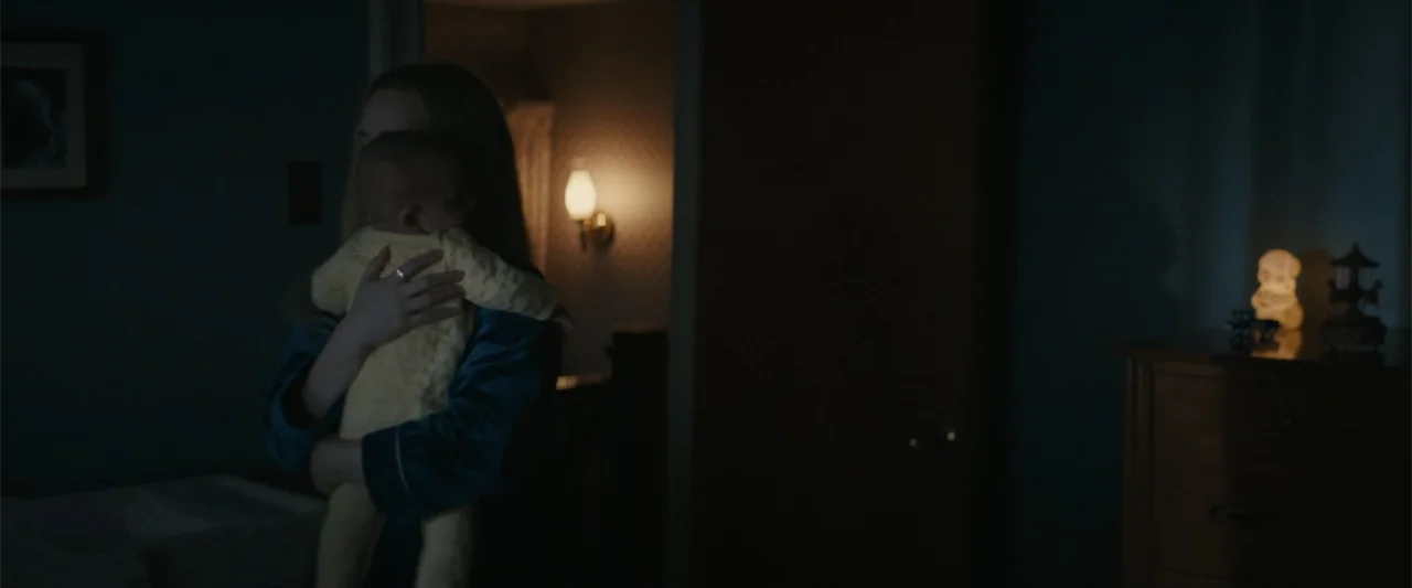 I'm Your Woman (2020) movie still: medium — A dimly lit room at night contains a dark wooden dresser and wall lamps. A woman wearing blue pajamas…