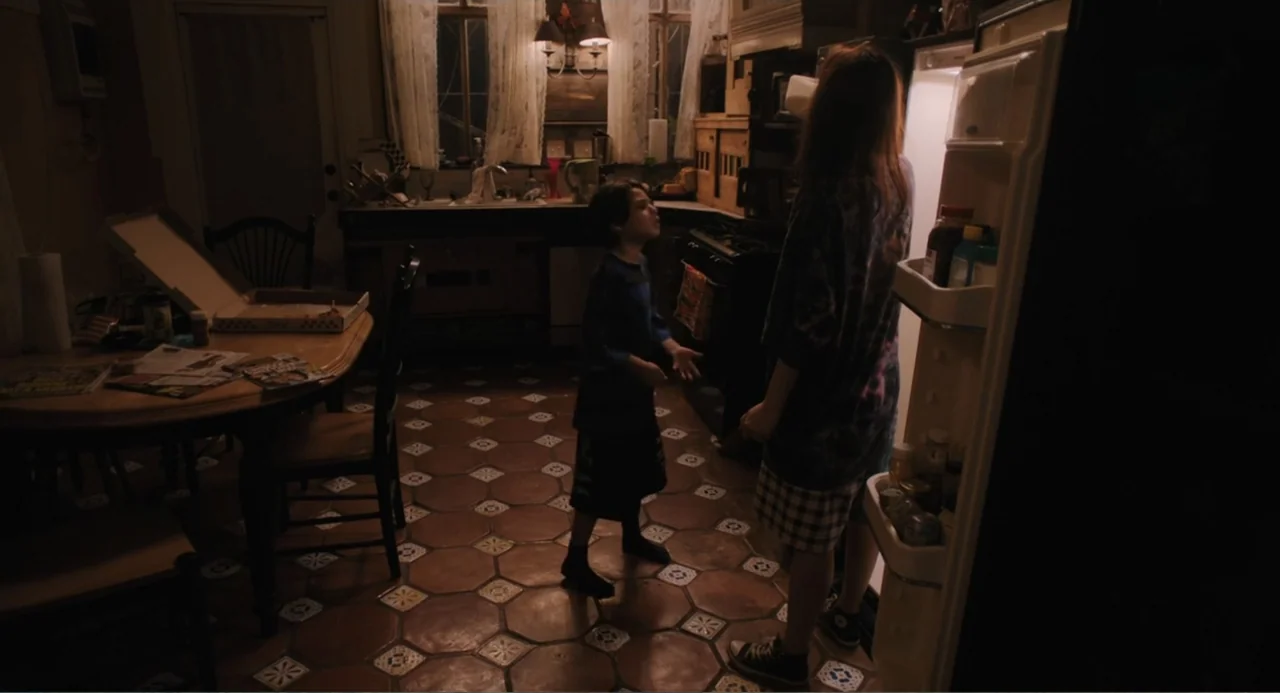 Mona Lisa and the Blood Moon (2022) movie still: medium — A dimly lit kitchen features terra-cotta hexagonal floor tiles and an open refrigerator…