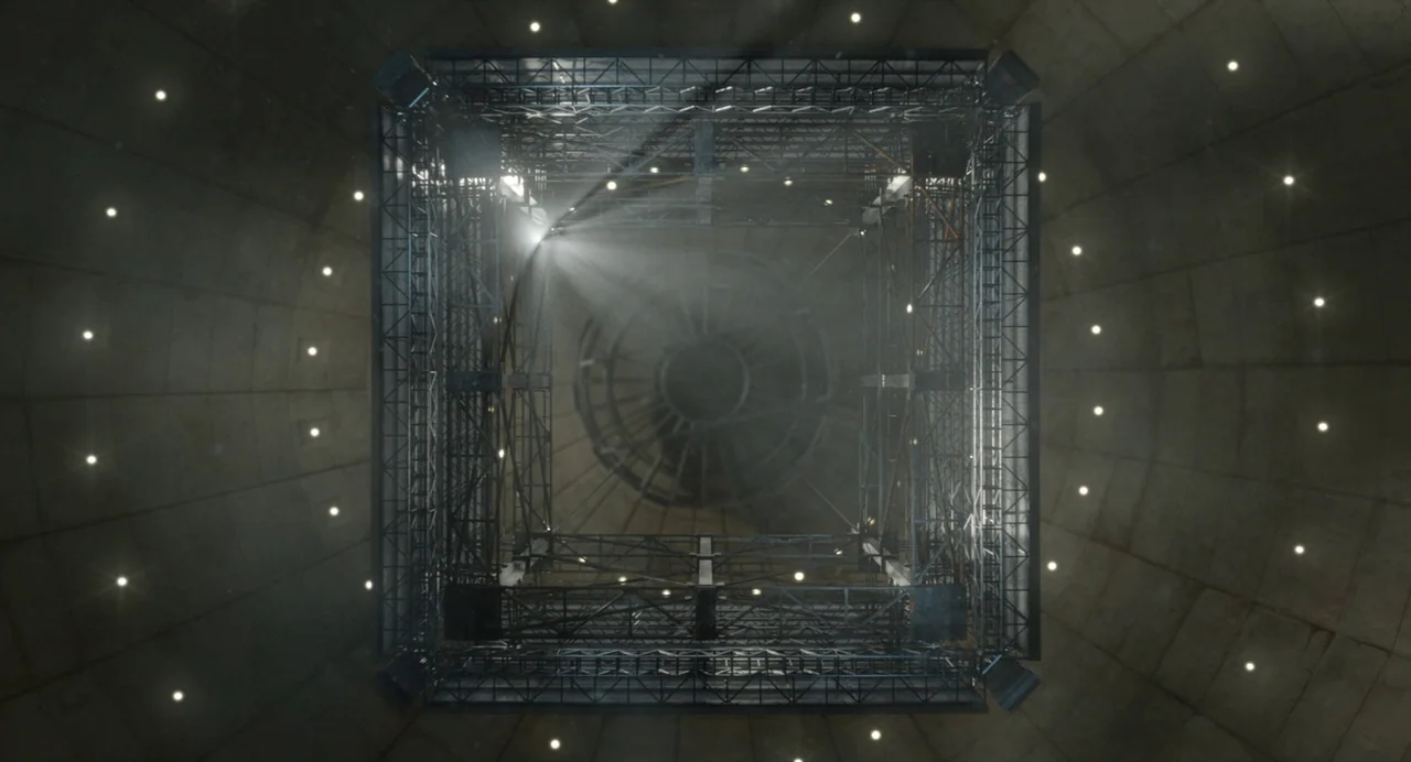 Beau Is Afraid (2023) movie still: establishing — A view looking directly down into a deep, circular concrete industrial shaft. A large square metal…