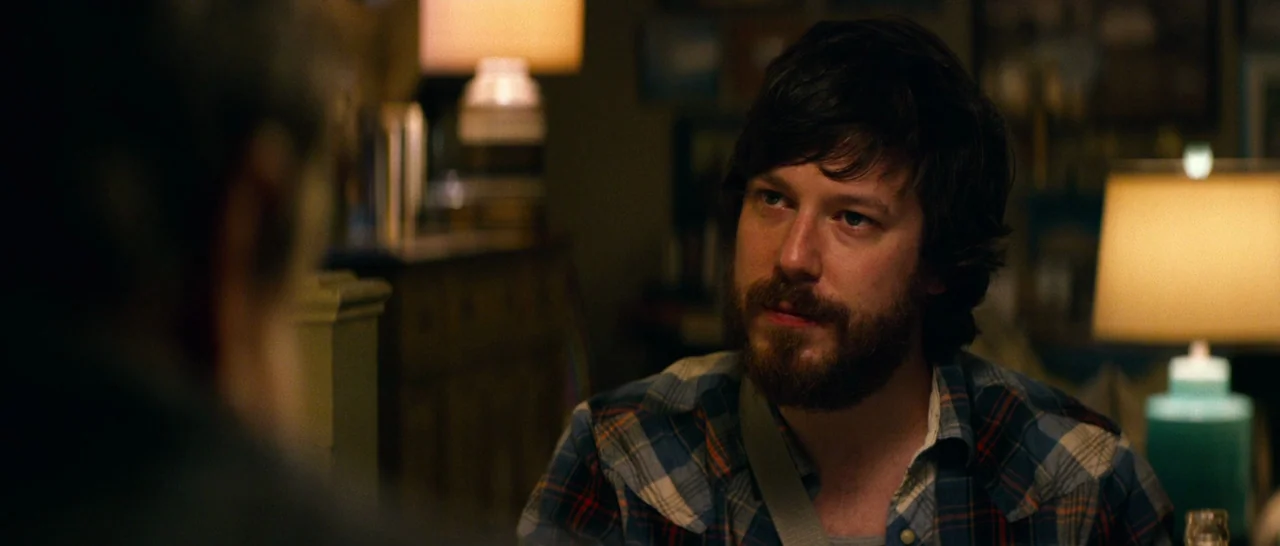 10 Cloverfield Lane (2016) movie still: medium — A dimly lit room with table lamps providing warm light against dark shadows. A man with a beard in…