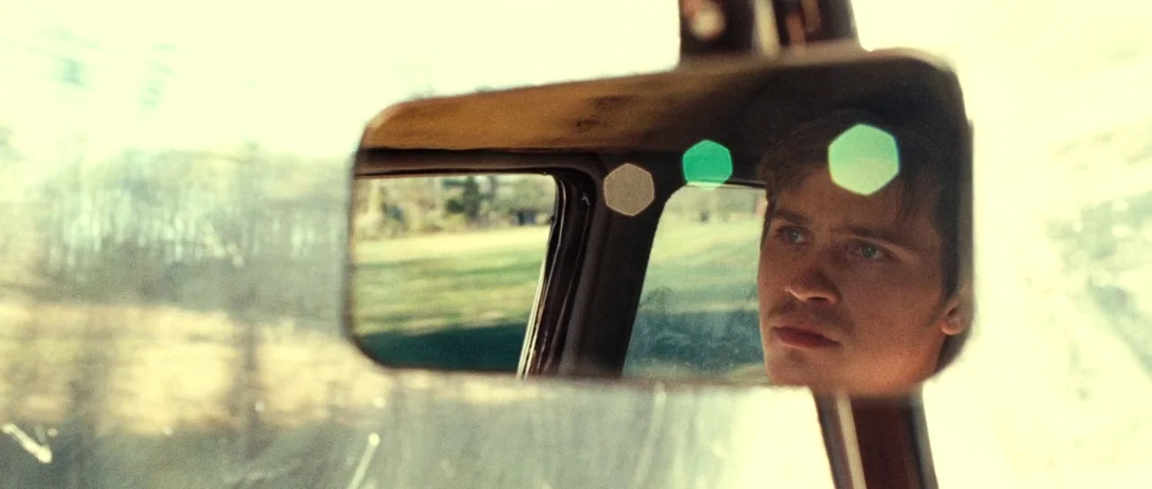 On The Road (2012) movie still: closeup — The interior of a vehicle seen through the perspective of a rear-view mirror. A young man's face is…