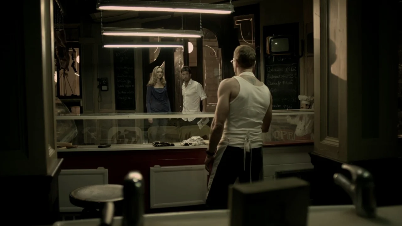 6 Bullets (2012) movie still: medium — A dimly lit butcher shop features display counters and chalkboard menus on the walls. A man in an apron…