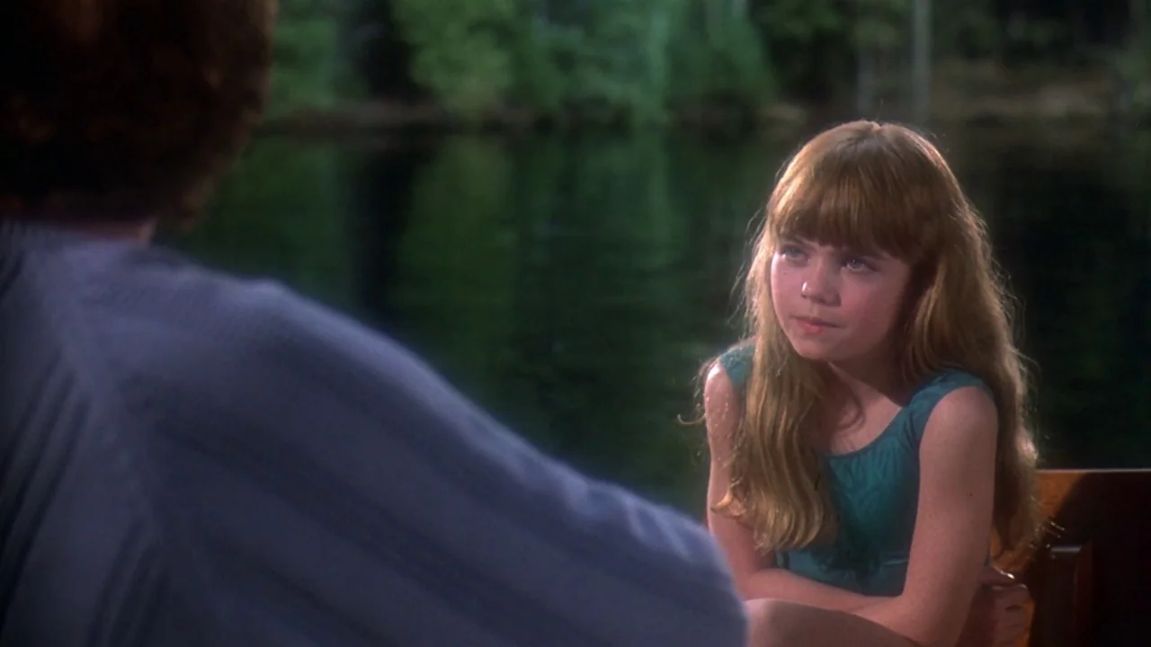Friday the 13th Part VIII: Jason Takes Manhattan (1989) movie still: medium — A young girl is positioned in front of a dark, calm lake shoreline.…