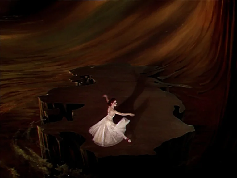 The Red Shoes (1948) movie still: wide — A dancer performs on a small wooden platform surrounded by dark, abstract textured scenery. The elevated…