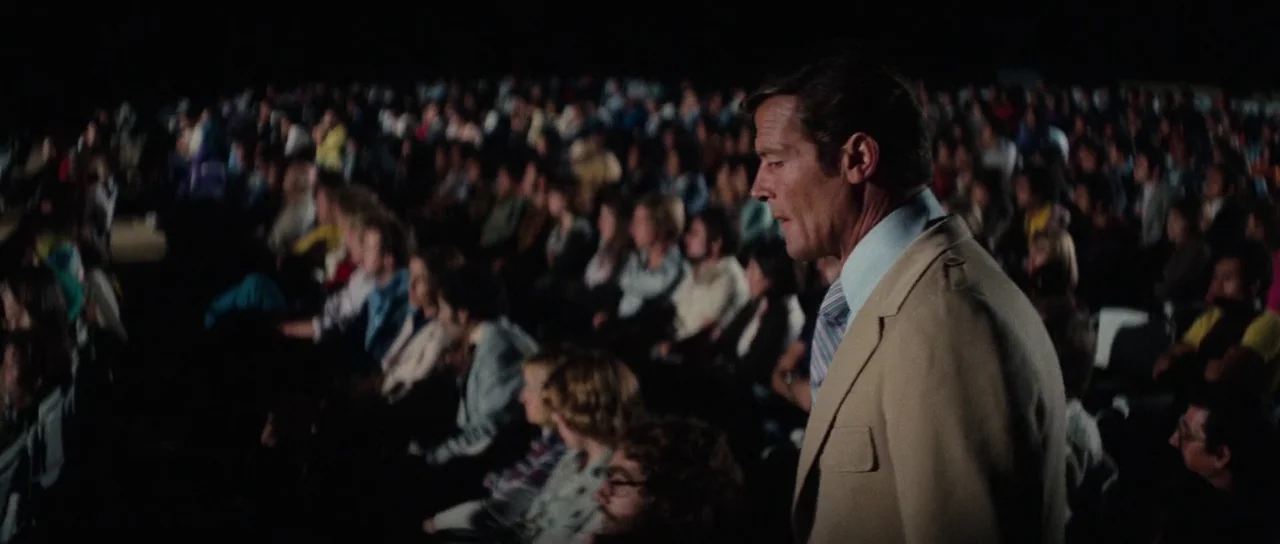 The Spy Who Loved Me (1977) movie still: medium — A dark movie theater auditorium is filled with rows of seated, obscured patrons. A man in a beige…