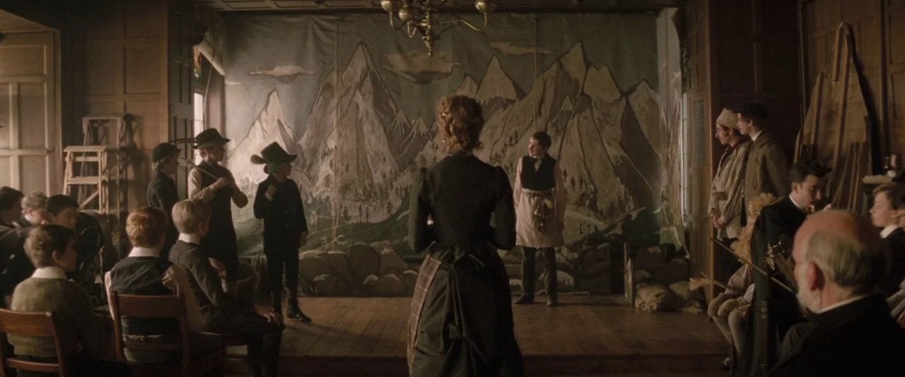 The Invisible Woman (2013) movie still: wide — A wooden interior hall features a makeshift stage with a painted mountain backdrop. A woman in a…