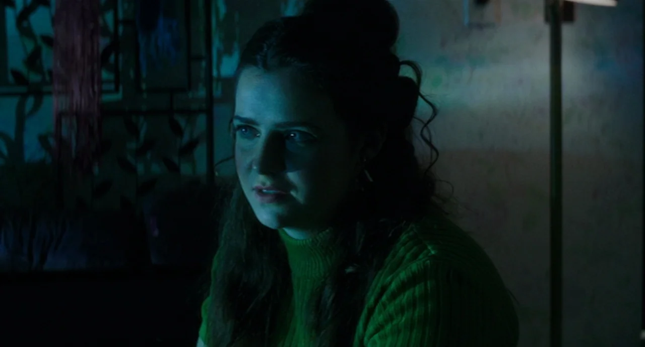 Ouija: Origin of Evil (2016) movie still: closeup — A dimly lit room at night with a screen casting a blue glow. A young woman in a green top looks…