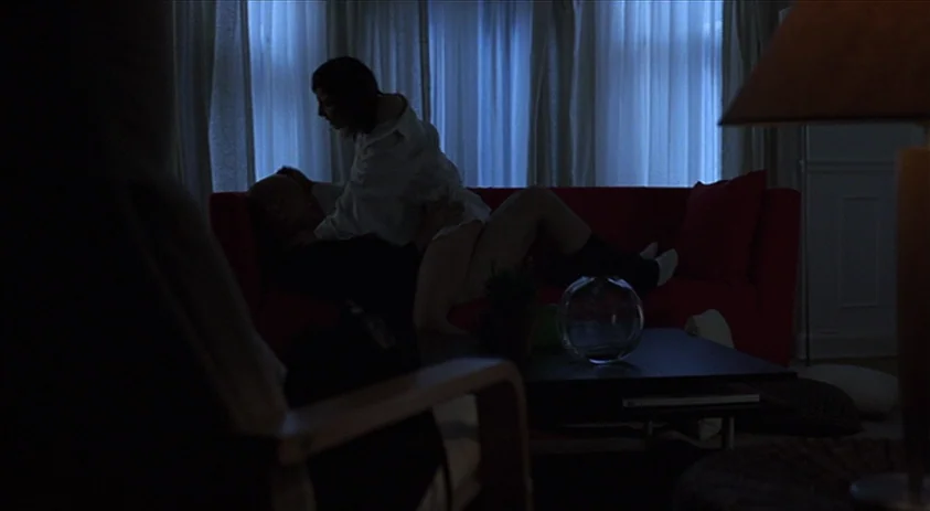 Being John Malkovich (1999) movie still: medium — A dark living room features a bright red sofa placed before a large window. A man and a woman are…