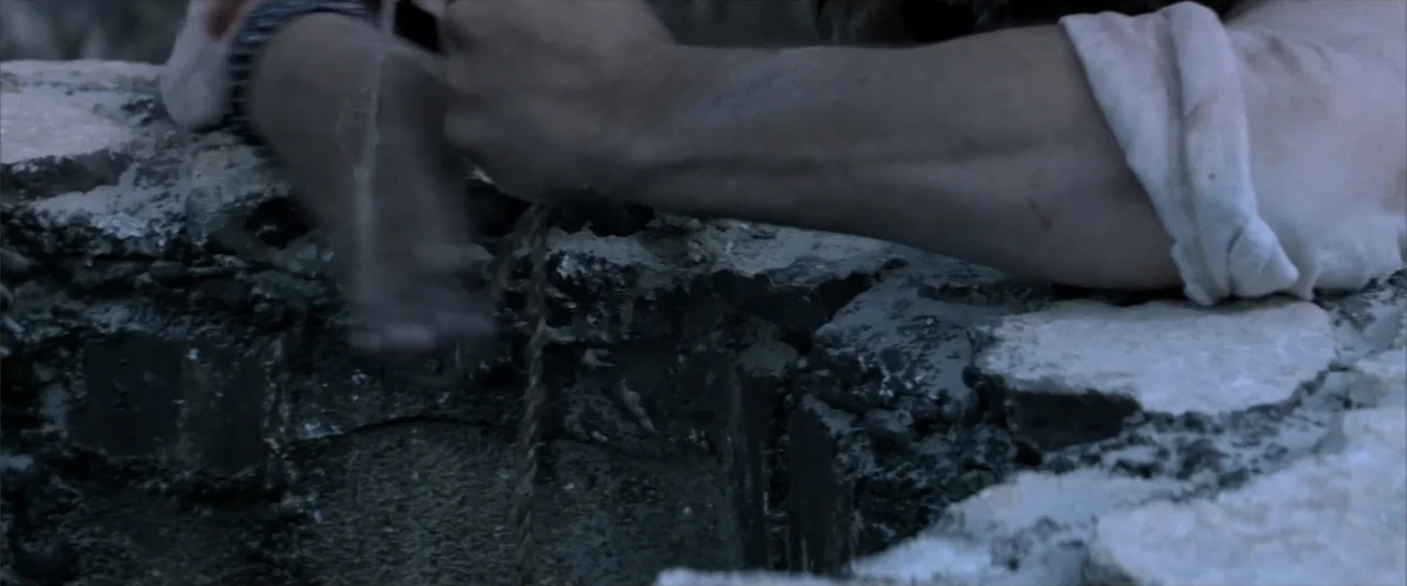 Matar o morir (1984) movie still: closeup — A weathered circular stone well made of stacked jagged blocks sits in daylight. A rough woven rope hangs…