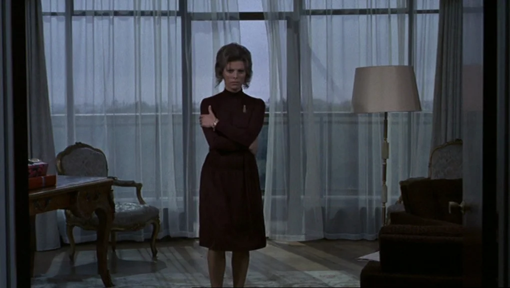 Frenzy (1972) movie still: fullbody — A spacious room features large windows draped with floor-length white curtains. A woman in a dark dress stands…