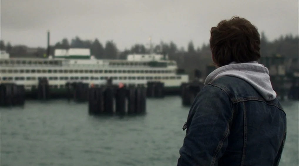 Your Sister’s Sister (2011) movie still: medium — An overcast waterfront with a large ferry docked behind a row of wooden pilings. A young man…