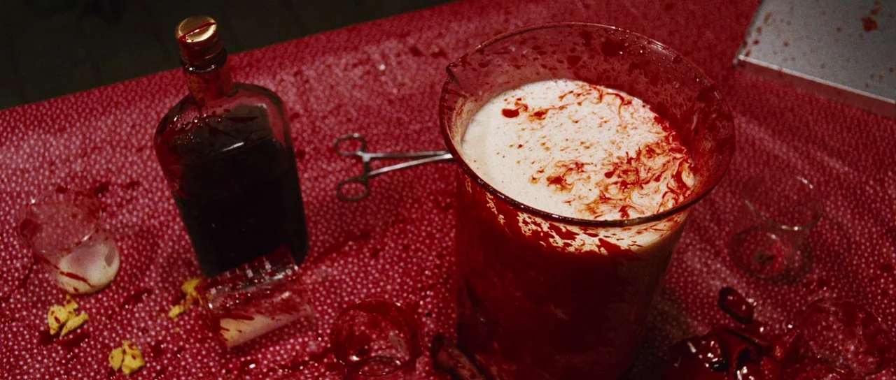 Black Christmas (2006) movie still: closeup — A table covered in a red polka-dot cloth is stained with blood splatters. A glass beaker filled with…