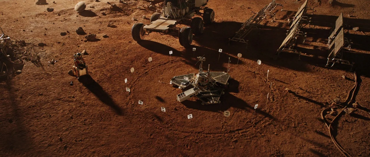 The Martian (2015) movie still: wide — A desolate reddish Martian landscape features a lander surrounded by a circular array of markers. A solitary…