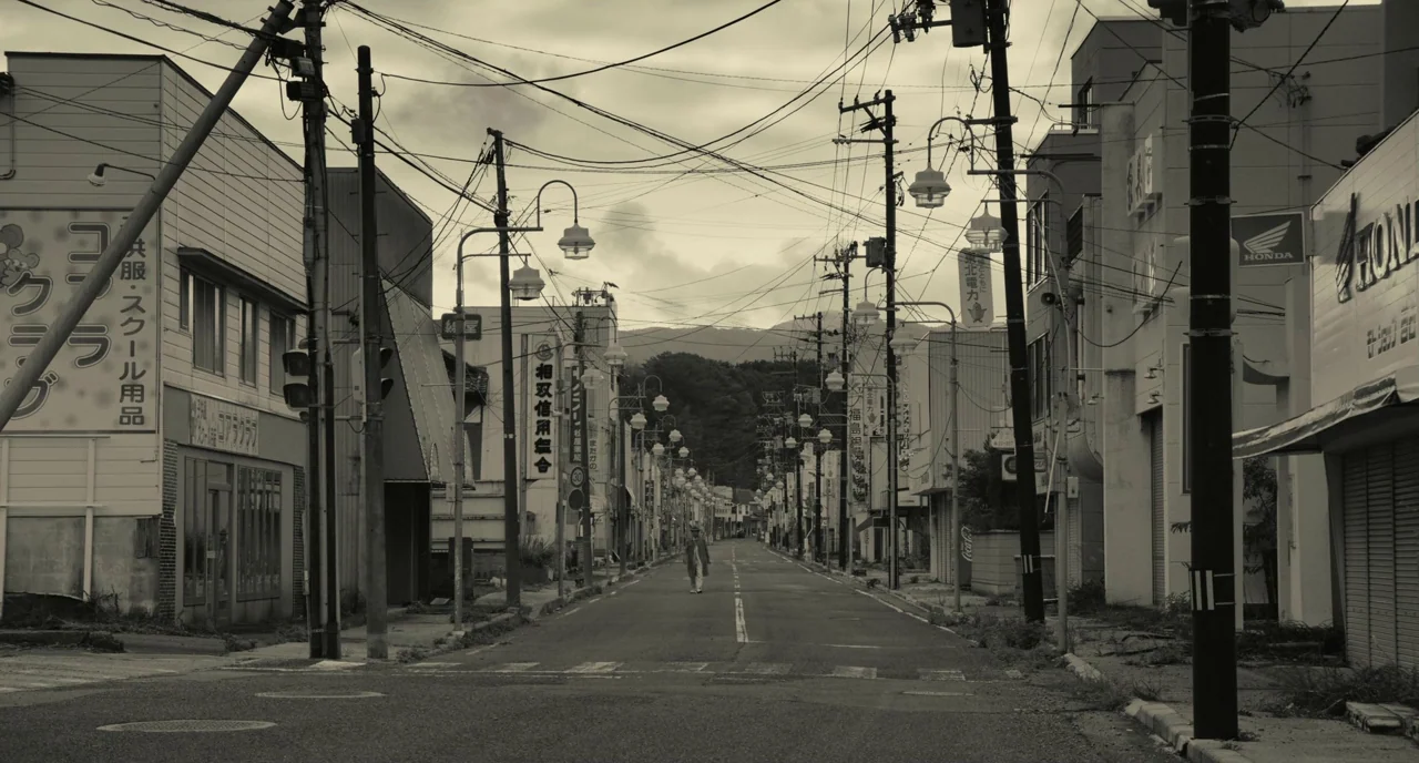 The Whispering Star (2015) movie still: wide — A deserted street in a Japanese town lined with utility poles and overhead wires. A lone person walks…