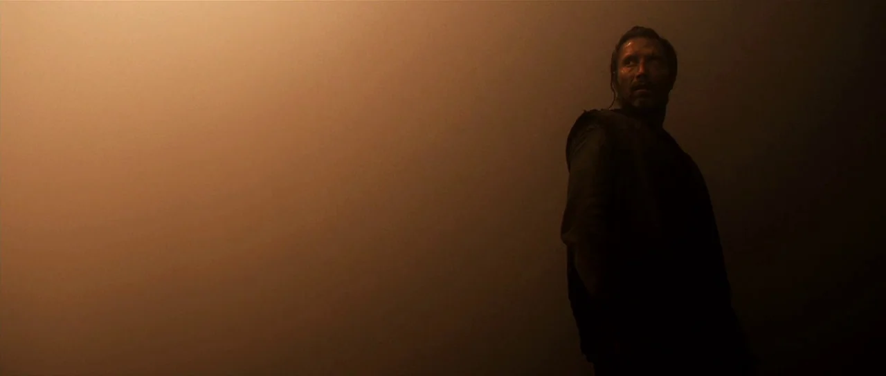 Valhalla Rising (2009) movie still: medium — A dark space filled with heavy brown fog obscuring the depth of the background. A man stands in the…