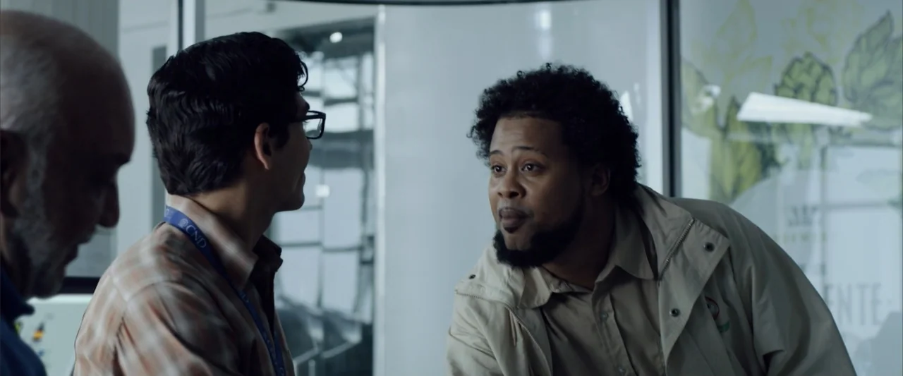 La Musiquita por Dentro (2019) movie still: medium — An office interior features glass partitions and a printed wall graphic in the background.…