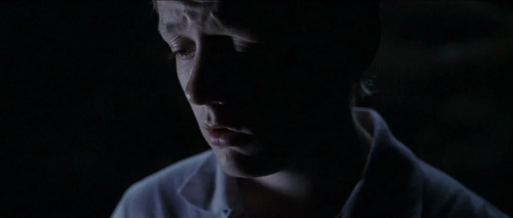 The Scouting Book for Boys (2009) movie still: closeup — A man stands in an dark interior environment with minimal ambient light. He looks downward…