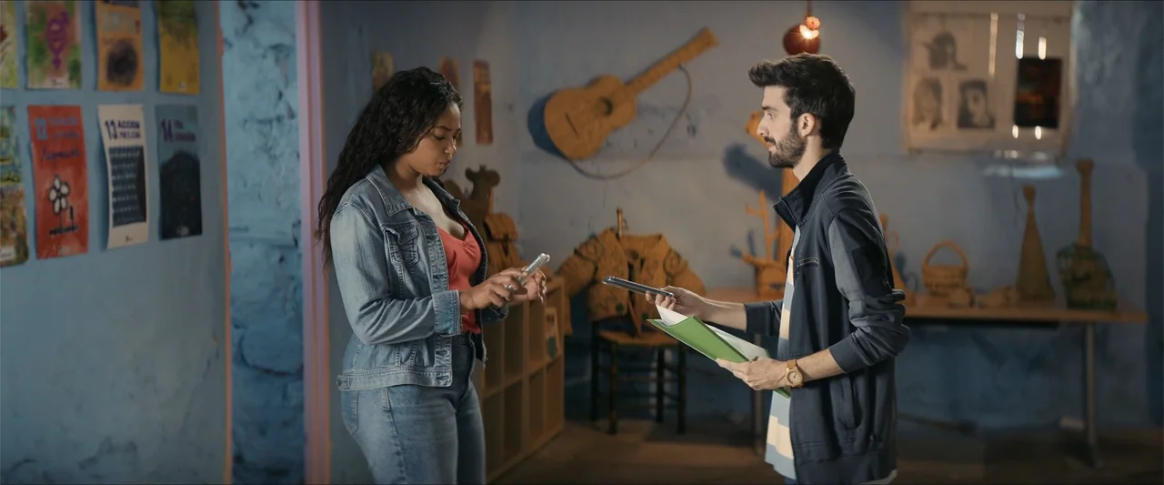 A Hipster in Rural Spain (2024) movie still: medium — A community center interior has light blue textured walls decorated with colorful paper…