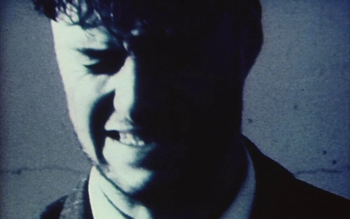 The Last of England (1987) movie still: closeup — A close portrait of a man in a dimly lit, nondescript interior space. The subject pulls back his…