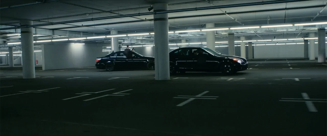 Gunpowder Milkshake (2021) movie still: wide — A spacious underground concrete parking facility features marked stalls and rows of support pillars.…