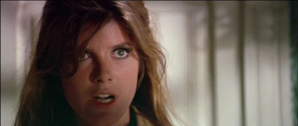 The Graduate (1967) movie still: closeup — A woman stands in a bright indoor space with paneled walls. The subject gazes off-camera with her mouth…