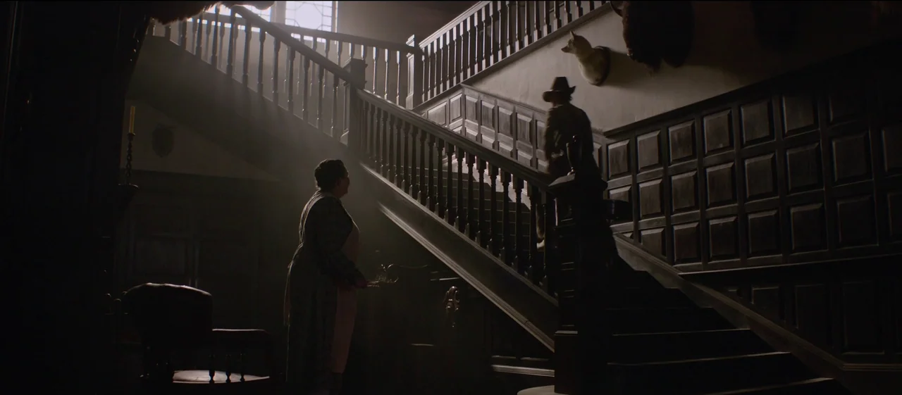 The Power of the Dog (2021) movie still: wide — An opulent Victorian staircase features dark wood paneling and taxidermy mounts on the walls. A…