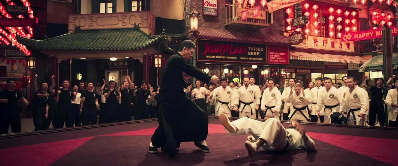 Ip Man 4: The Finale (2019) movie still: fullbody — A crowded Chinatown street at night features red lanterns and storefront signs overhead. A man…