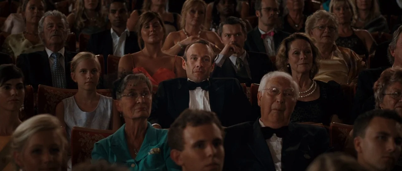 Sound of Noise (2010) movie still: wide — An audience sits in rows of velvet seats inside a large, ornate performance theater. The diverse group of…