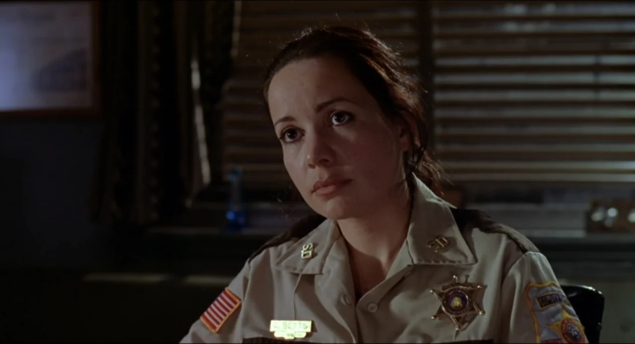 Cop Land (1997) movie still: medium — A dimly lit office interior features horizontal window blinds providing the primary light source. A female…