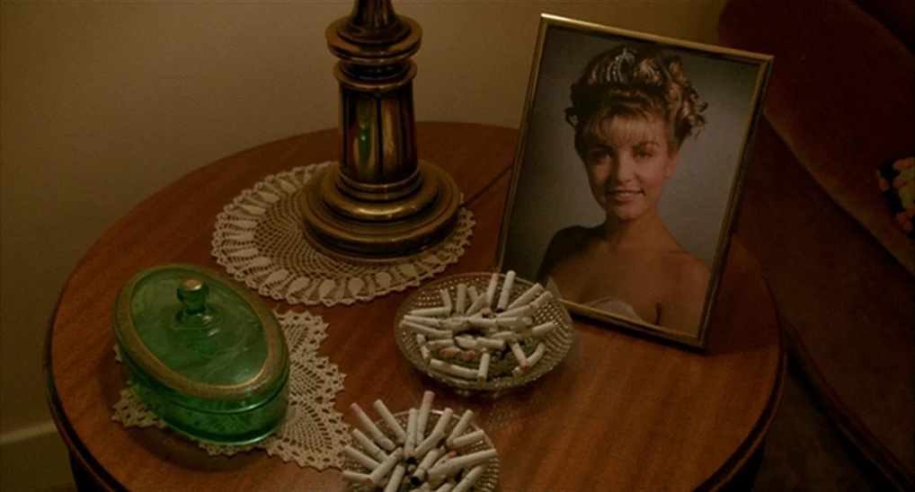 Twin Peaks: Fire Walk With Me (1992) movie still: closeup — A wooden end table holds a lamp, two glass ashtrays, and a green jar. A framed portrait…