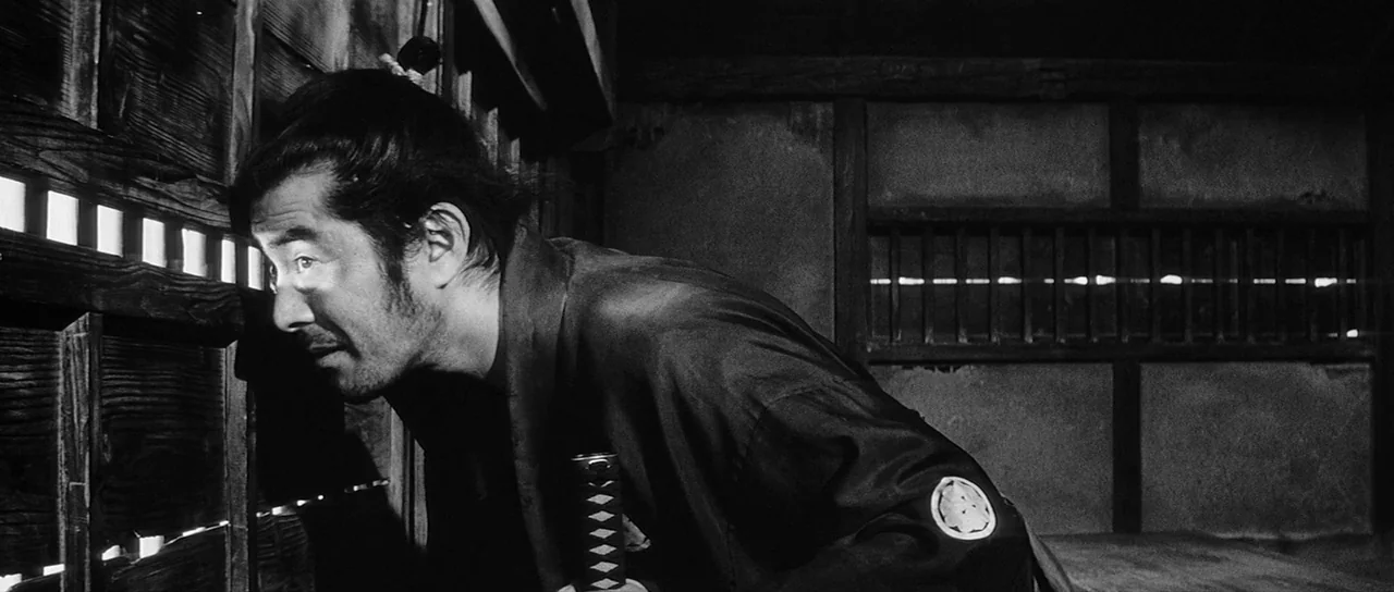 Yojimbo (1961) movie still: medium — An interior wooden room features walls constructed with horizontal wooden slats for ventilation. A man in…