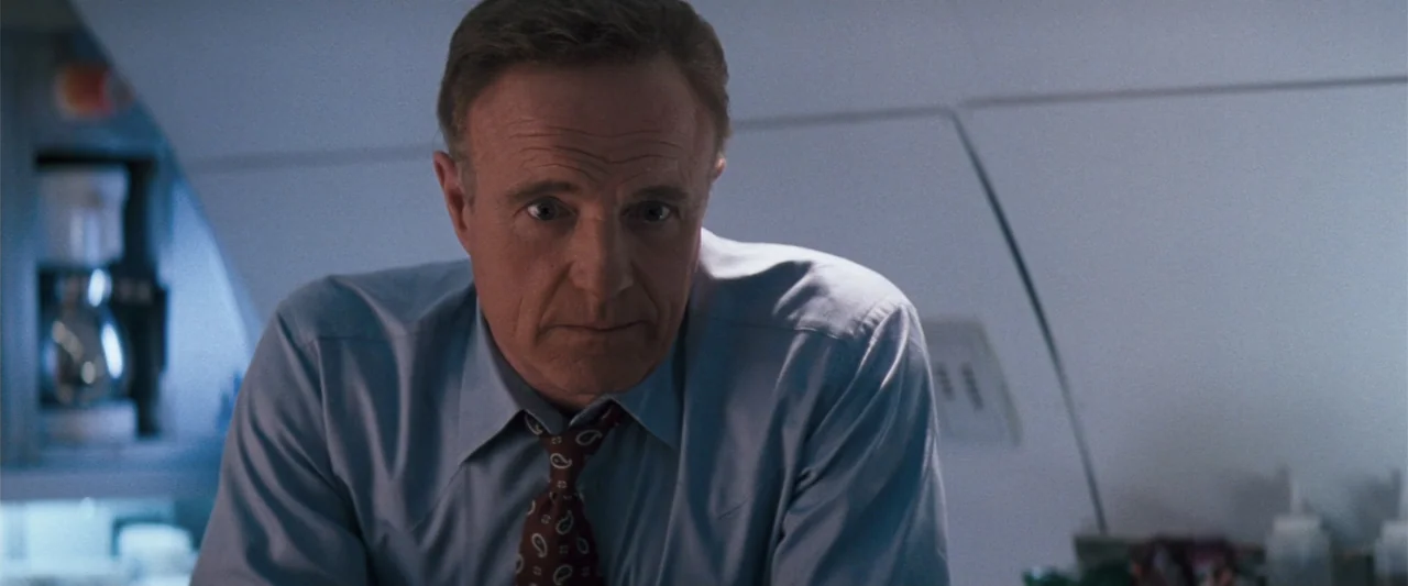 The Eraser (1977) movie still: medium — A cramped and sterile airplane galley with white paneling and hidden galley equipment. A middle-aged man in…