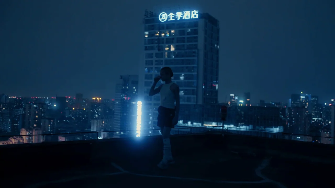 The Last Year of Darkness (2023) movie still: fullbody — A dark rooftop overlooking a sprawling urban landscape at night with illuminated high-rise…